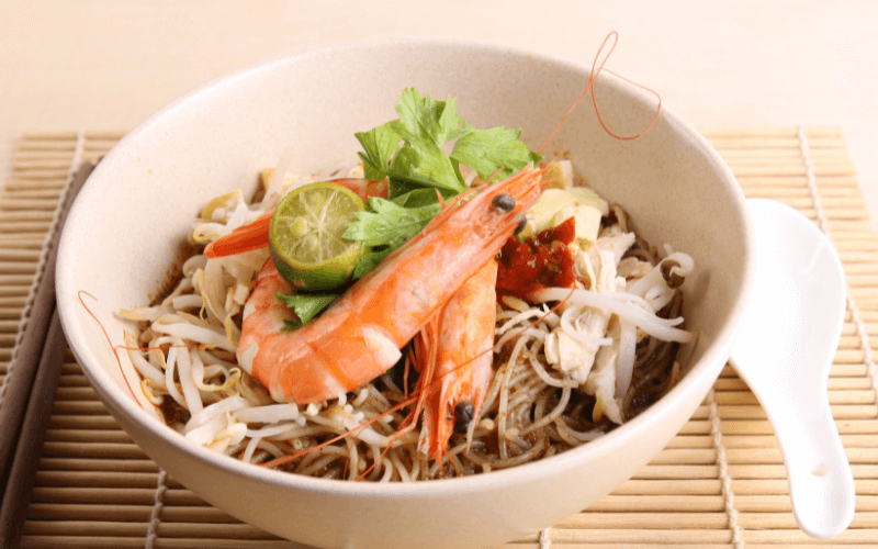 Image of Laksa noodles surrounded by plates of prawns, fish cakes, etc.