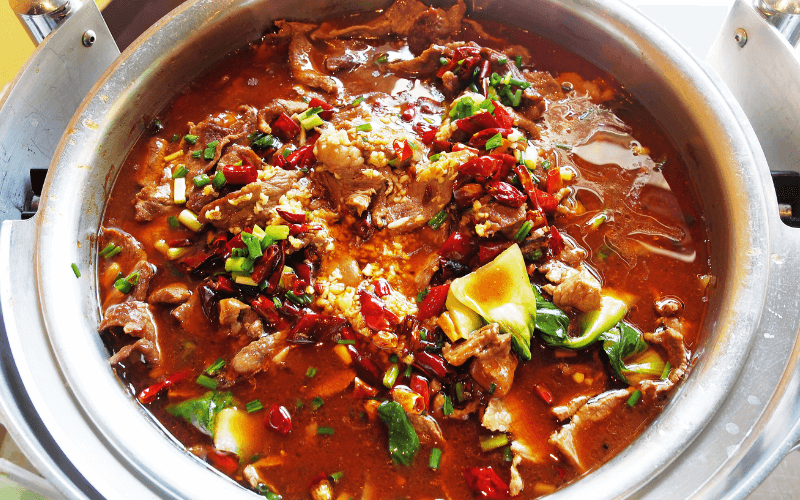 Feel The Burn From Singapore’s Spiciest Dishes Image of a bowl of meat with plenty of red chilli peppers. It’s on a table with utensils ready to be served or eaten