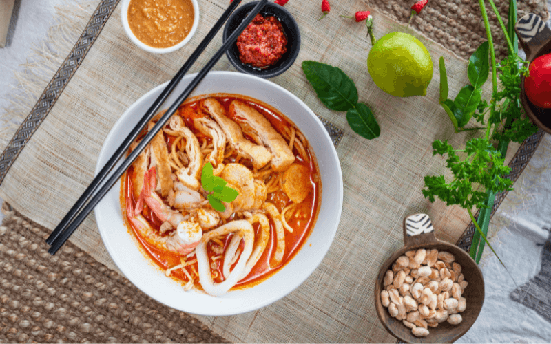 Image of an upward shot of a bowl of Laksa, with chopsticks and a soup spoon