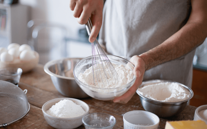 8 Must-Have Baking Tools And Gadgets For Beginners and Pros Man whisking flour in a glass bowl