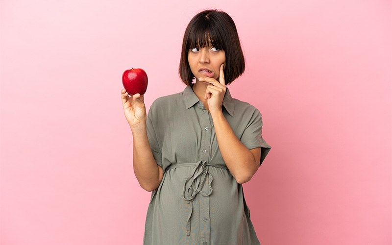 A person holding an apple, thinking of whether or not they should eat it.