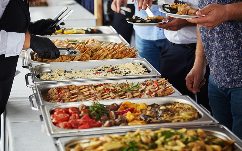 Servers putting food on people’s plates at a buffet.