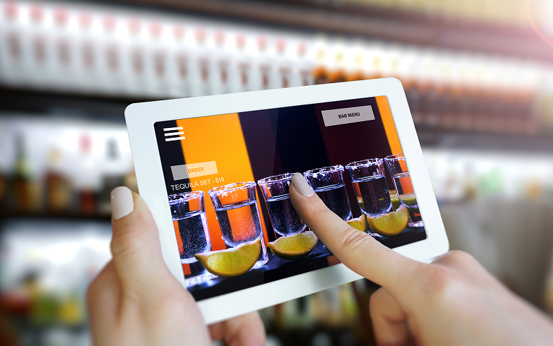 The Tech Evolution in Modern Cocktail Bars A customer selecting a cocktail from a digital touchscreen interface.