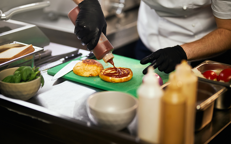 Chef assembling a gourmet nasi lemak burger in a modern kitchen.