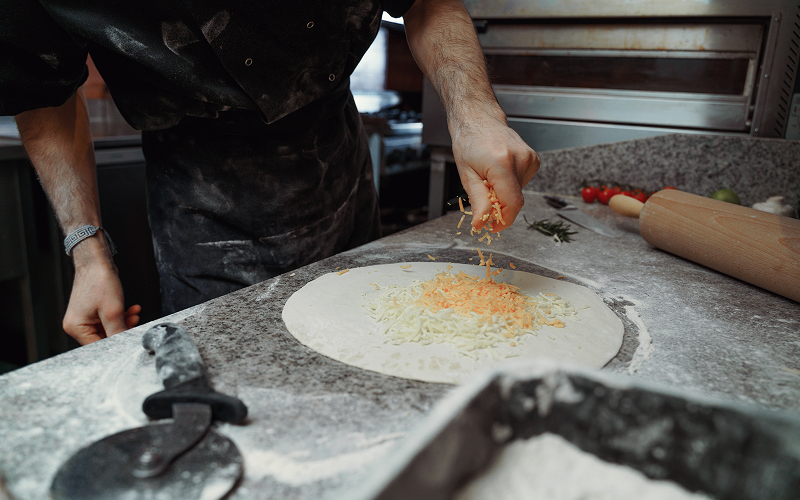 Image of a pizza kitchen with a baker making a pizza