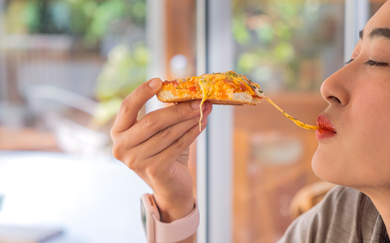 15 Essential Kitchen Gadgets That Help Create the Best Pizza Image of a person eating a slice of pizza.