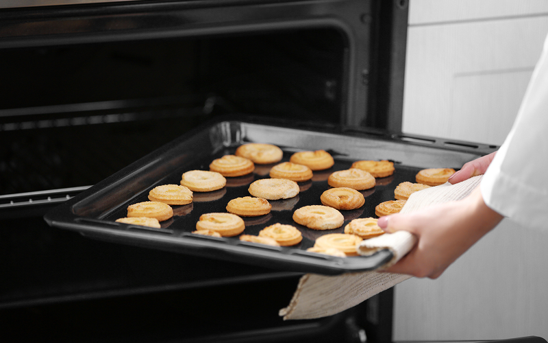 The Smart Tools and Machines Powering Bakers in Singapore Image of a baker taking out a tray of baked goods from an oven